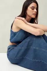 Falda midi de denim negro con tiro bajo, corte evasé, costuras verticales y ruedo desflecado.