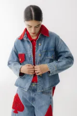 Campera de jean celeste con detalles de crochet rojo en cuello, bolsillo y ruedo. Tiene cierre frontal con botones dorados, bolsillos laterales y corte holgado.