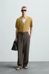 Pantalón marrón de corte ancho, con cintura ajustable con cordón, bolsillos delanteros y traseros tipo parche, detalle de costuras verticales en el frente y cierre frontal con cremallera y gancho metálico oculto.