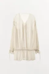 Top semitransparente color crema, de escote pico ajustable con lazadas, manga larga con aberturas y puño ajustable con cordones.