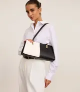 Cartera shoulder mediana de cuero sintético, con diseño bicolor blanco y negro y detalles metálicos dorados.