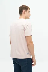 Remera color rosa pálido de manga corta con cuello redondo y estampado frontal con texto y diseño floral en tonos azules.