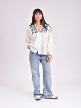 Camisa blanca de manga larga con bordado negro en el cuello y puños, con botones frontales.