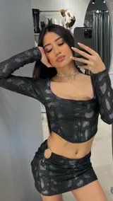 Conjunto negro brillante con estampado animal print, compuesto por un top de mangas largas con escote cuadrado y una minifalda con detalle de aro metálico en la cadera.