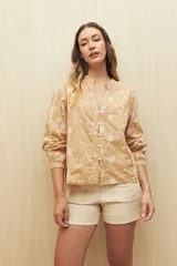 Camisa color beige con bordado floral blanco en toda la superficie. Presenta cuello mao, escote en V y abotonadura frontal, con mangas largas terminadas en puño angosto.