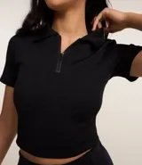 Blusa negra de poliéster con elastano, modelo polo, con cremallera en el cuello, manga corta, texturizada y seamless.