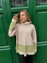 Sweater beige de tejido grueso con cuello alto, corte oversize y tajo a los lados. Tiene rayas horizontales verdes en el ruedo y en los puños.