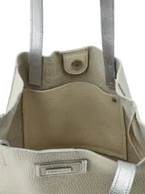 Bolso tipo tote bag color beige con base plateada, doble asa de hombro plateada y logo de la marca en el frente.