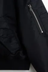 Campera bomber de nylon color negro con corte holgado y levemente acolchada. Cuenta con cuello de peluche al tono, cierre frontal metálico, bolsillos laterales con solapa y un bolsillo con cierre en la manga. Posee puños y bajo acanalados.