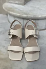Sandalias de cuero color champagne, con punta cuadrada, tira ancha sobre el empeine y tira al tobillo con hebilla metálica. Taco cuadrado de 7 cm.