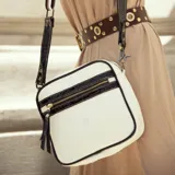 Morral de cuero vacuno en colores blanco, negro y marrón, con correa larga ajustable y bolsillo exterior con cierre.
