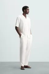 Camisa de calce relajado confeccionada en tejido fluido de mezcla de viscosa, color blanco. Presenta cuello bowling, manga corta, aberturas laterales en el bajo y cierre frontal con botones al tono.