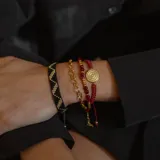 Pulsera tejida roja con dije circular dorado con diseño geométrico y un cristal incrustado.