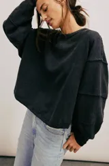 Camiseta de manga larga negra con textura acanalada y silueta holgada. Presenta escote redondo, hombros caídos y puños, con costuras marcadas y terminaciones sin rematar.