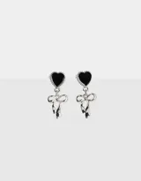 Par de aros colgantes plateados, con pasante de corazón negro y dije de moño.