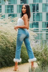 Pantalón de denim celeste con corte acampanado y detalle de plumas blancas en el ruedo.