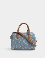 Cartera bowling de denim celeste con estampado de flores blancas, doble asa corta de cuero marrón y correa larga regulable y desmontable.