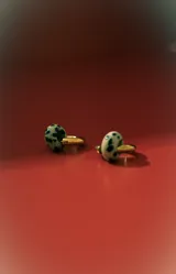 Aros tipo argolla de metal dorado con un dije colgante en forma de cuenta ovalada con estampado dálmata (blanco y negro).