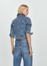 Chaqueta de jean azul de corte clásico, con cuello camisero, mangas 3/4 con puños arremangados, cierre frontal con botones metálicos, bolsillos de parche con solapa abotonada en el pecho y bolsillos laterales.