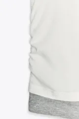 Camiseta blanca de corte slim fit, cuello redondo y manga corta con acabados en puntilla. Tiene detalle de frunces en los laterales y tejido combinado a contraste efecto doble en cuello, mangas y ruedo.