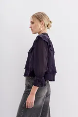 Camisa azul de algodón con bordados a tono, cuello alto, mangas largas abullonadas con puños elásticos y volados en el canesú delantero y trasero.