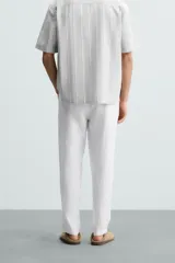 Pantalón de vestir blanco, confeccionado en lino, de corte recto, con bolsillos laterales y traseros. Se ajusta a la cintura con botón y cierre.
