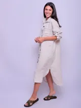 Vestido camisero largo de lino color beige, con cuello clásico, manga larga con puños abotonados y cierre frontal con botones. Tiene un bolsillo de parche en el pecho.