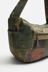 Bolso de hombro tipo bandolera con estampado de parches de denim en tonos verdes, marrones y azules. Tiene un compartimento principal con cierre de cremallera, un bolsillo interior con cremallera y un bolsillo trasero con cremallera. El asa de hombro es ajustable.