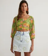 Blusa corta de tul con estampado de hojas y frutas, escote cuadrado, mangas largas con elástico en hombros y puños, y flecos en el frente.