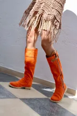 Botas altas color naranja de gamuza, con cierre lateral y hebilla decorativa en la parte superior.