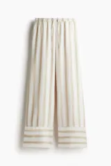 Pantalón de lino color crudo con rayas verticales color beige. Corte holgado, cintura elástica con cordón ajustable y piernas anchas extralargas.