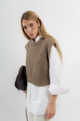 Chaleco de lana color crema, tejido a punto perlado con calado en la parte delantera. Tiene cuello a la base y silueta cuadrada.