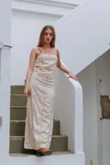 Vestido largo color crema con tirantes finos y corte debajo del busto. Presenta costuras verticales a lo largo del vestido y un corte a la altura de la rodilla.