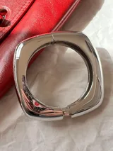 Brazalete rígido dorado con forma cuadrada y cierre a presión.