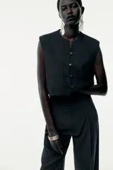 Top tipo chaleco negro de Zara Woman Collection, con cuello redondo y sisa. Presenta costuras a contraste y cierre frontal con botones.