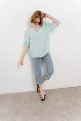 Camisa azul de lino con escote en V abotonado, bolsillo frontal y mangas 3/4 con trabilla.