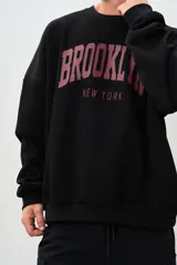 Buzo negro de corte holgado con estampa frontal de letras en color borgoña que dice "BROOKLYN" y "NEW YORK".