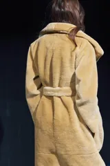 Abrigo largo color camel con efecto piel de oveja, cuello solapa, manga larga, bolsillos delanteros y cinturón ajustable con lazadas. Forro interior.