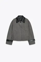 Chaqueta corta de tweed gris con cuello solapa y puños de cuero negro. Cierre frontal con botones ocultos.