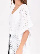 Blusa blanca con calados y mangas cortas amplias, con lazo de ajuste en la cintura.