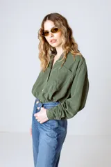 Camisa verde militar de manga larga con cuello camisero, cierre frontal con botones, dos bolsillos con solapa en el pecho y puños abotonados.