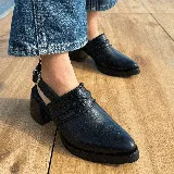 Zuecos negros de cuero con punta fina, taco cuadrado y tira trasera con hebilla. Presentan detalle de trenzado en el empeine.