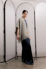 Ruana color gris claro con flecos en el borde inferior y etiqueta de cuero con logo en la parte delantera.