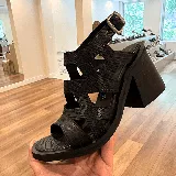 Sandalia negra de cuero con textura de piel de serpiente, diseño de tiras entrecruzadas y hebilla ajustable en el tobillo. Posee una plataforma gruesa y un taco ancho y alto.
