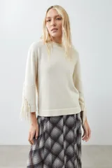Sweater beige claro de tejido de punto con cuello redondo y mangas largas con flecos.