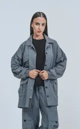 Campera gris con broches en el delantero, forrada con red, múltiples bolsillos con detalles en réflex y puños elásticos en las mangas. Confeccionada en textil liviano 100% poliéster y calce oversize.