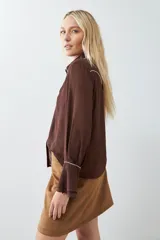 Camisa marrón de mangas largas con botones y detalles de pespuntes blancos en cuello, solapa y canesú.