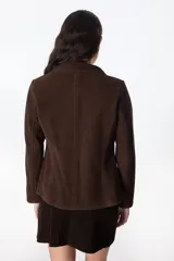 Chaqueta marrón de cuero vacuno descarne, con cuello camisero, corte entallado con pinzas y mangas sastre. No tiene botones.