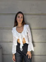 Blusa de encaje blanco con volados en el escote y mangas acampanadas. Se ata en el frente con lazos.