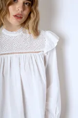 Blusa blanca de mangas largas con cuello alto con volados y detalles de encaje.